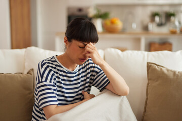 Young Asian woman with headache sitting on couch at home