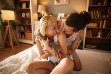 Tattooed man and beautiful woman embracing at home in bed 
