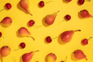Colorful food pattern made of pears and cherries on yellow background. Flat lay.