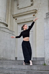 Young woman in black outfit performing a contemporary dance move on stone stairs