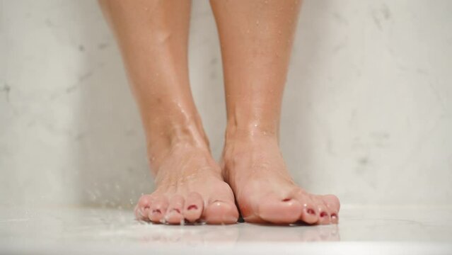 Naked Woman's Legs in the Shower with White Marble Walls, water droplets falling down.