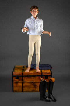A half-dressed male youth equestrian rider gleefully dances atop a box, instead of getting ready for his competition