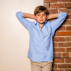 Portrait of a young male model standing against a wall with his hands behind his head