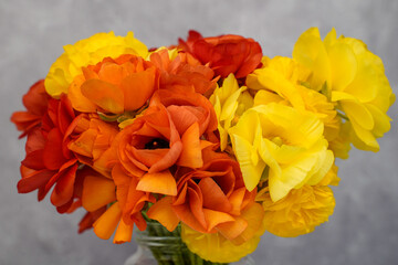 Bouquet of yellow and orange ranunculus flowers in a glass jar.