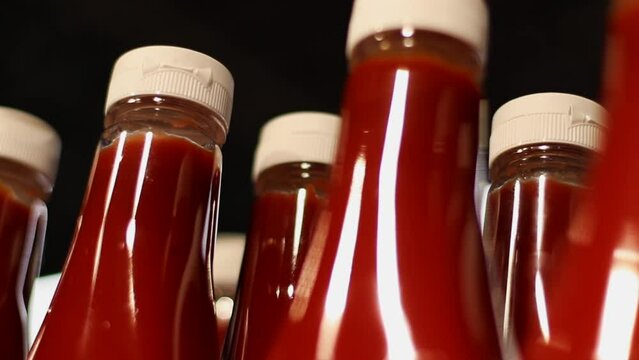 Many Plastic Bottles with Tomato Sauce or Ketchup on Supermarket Shelf on Black Background. Close-up