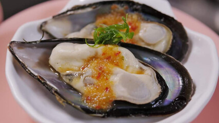 close-up of two mussels on a pink plate. There is a sauce drizzled on the mussels.