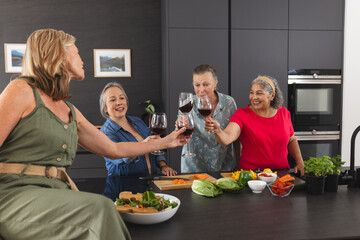 Group of senior women enjoying wine and preparing meal together in modern kitchen