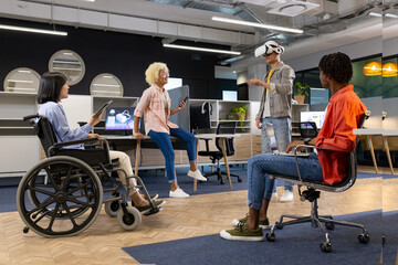 Obraz premium Business colleagues in office watching man using vr headset, asian woman in wheelchair, inclusivity
