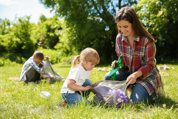 Fototapeta premium Mother and her children with plastic bags collecting garbage in park