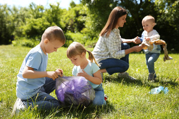 Fototapeta premium Mother and her children with plastic bags collecting garbage in park