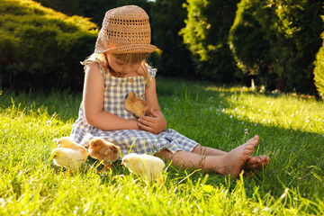 Little girl with cute chicks on green grass outdoors. Baby animals © New Africa