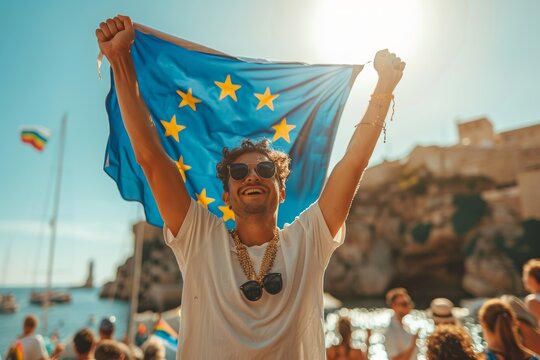 Young man joyfully celebrating under the sun while holding a European Union flag at a lively outdoor event by the seaside