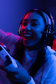 Happy biracial woman wearing headphones playing video games with controller