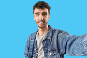 Handsome young man taking selfie on blue background, closeup