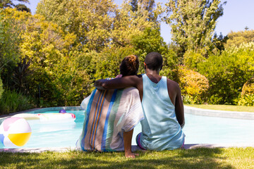 A diverse couple relaxes by pool, enjoying sunny summer day, vacation, and happiness