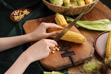 Woman cutting fresh corn cobs on wooden table