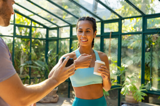 Biracial woman in athletic wear holding coffee cup paying with smartwatch - Powered by Adobe