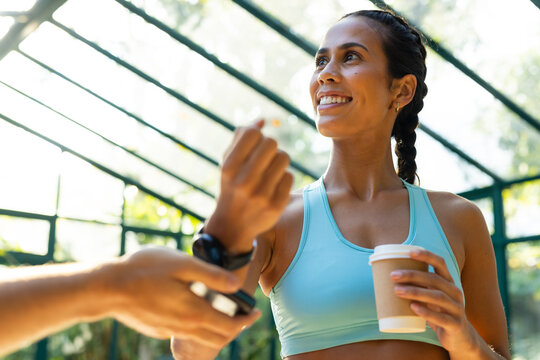 Biracial woman in athletic wear holding coffee cup paying with smartwatch - Powered by Adobe
