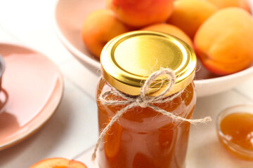 Jar with sweet apricot jam on white tile background