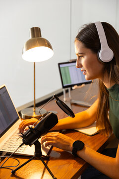 Smiling Caucasian woman with headphones recording podcast on laptop and microphone