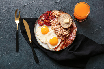 Plate with tasty English breakfast and glass of juice on black background