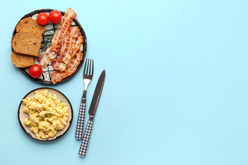 Plates of tasty scrambled eggs and bacon on blue background