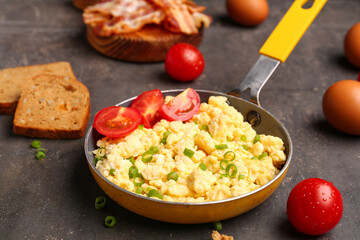 Frying pan of tasty scrambled eggs with tomatoes on grey background