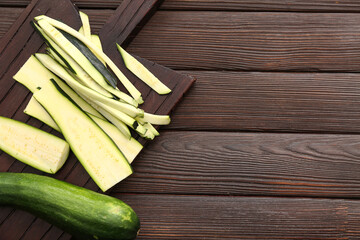 Board with slices of fresh green zucchini on wooden background