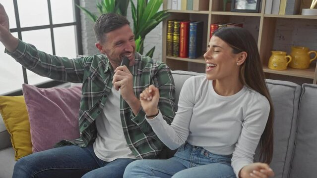 Hispanic man and woman joyfully singing with remote on sofa in a cozy living room.