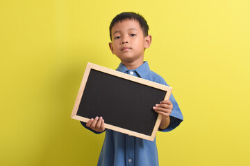 Cute little Asian boy holding a blank chalk board isolated on yellow background. Space for text, copy space, mockup banner
