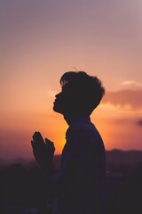 In the setting sun, the silhouette of a man with his hands clasped in prayer looks up at the sky and prays with his mouth closed. The serene expression symbolizes the deep connection between God and m