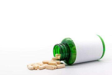 Yellow pills coming out of a green plastic bottle with blank label. Copy space. Medicine and health concept. selective focus