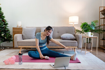 Woman Exercising at Home in Modern Living Room, Stretching on Yoga Mat with Laptop, Water Bottle, and Dumbbells, Cozy and Bright Interior with Sofa, Plants, and Christmas Tree