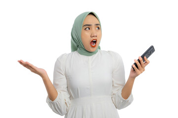 Surprised young Asian woman in green hijab and white blouse holding smartphone with open mouth and raised hand isolated on white background