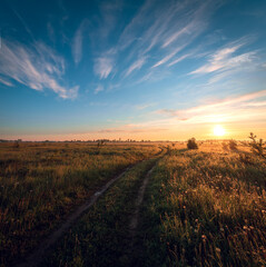 Obraz premium Rural road in a field against the backdrop of a summer sunset or sunrise.