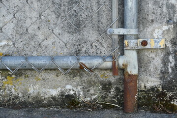 Corner of rusted chain link fence against cement wall.
