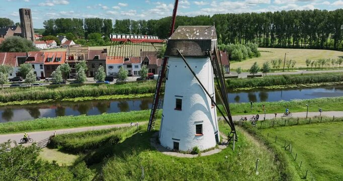 Damme, Belgium, June 2022. Drone orbits the scenic Schellemolen white windmill on a sunny day alongside the picturesque Damse Vaart canal.