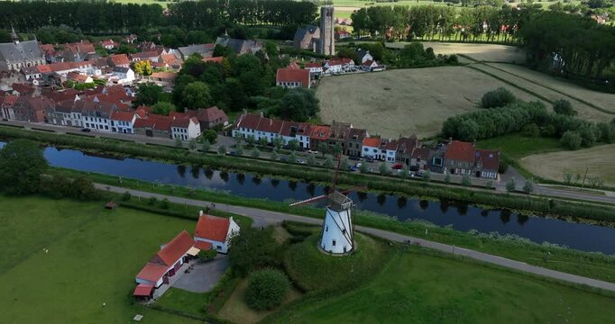 Damme, Belgium, June 2022. Drone orbits and pulls away from the scenic the Schellemolen white windmill on a sunny day alongside the picturesque Damse Vaart canal.