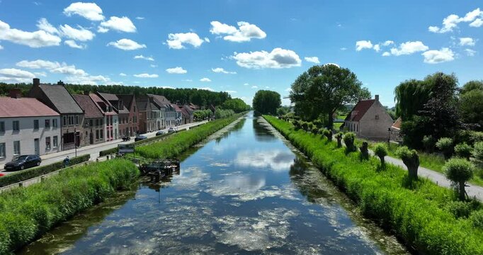 Damme, Belgium, June 2022. Drone pushes forwards above the Damse Vaart a picturesque canal under a bright blue sky with fluffy clouds.