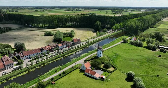 Damme, Belgium, June 2022. Drone orbits above the scenic Damse Vaart canal with the Schellemolen white windmill on a sunny day.
