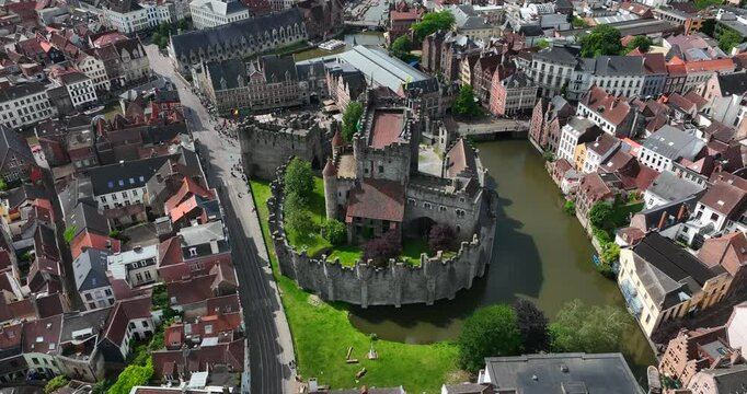 Gravensteen Castle, East Flanders, Ghent, Flemish Region, Belgium, June 2022. Drone high angle orbit right over Lieve Canal to reveal grassy lawn outside fortress.