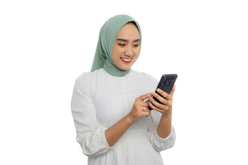 Happy young Asian woman in green hijab and white blouse using smartphone for messaging with friends...