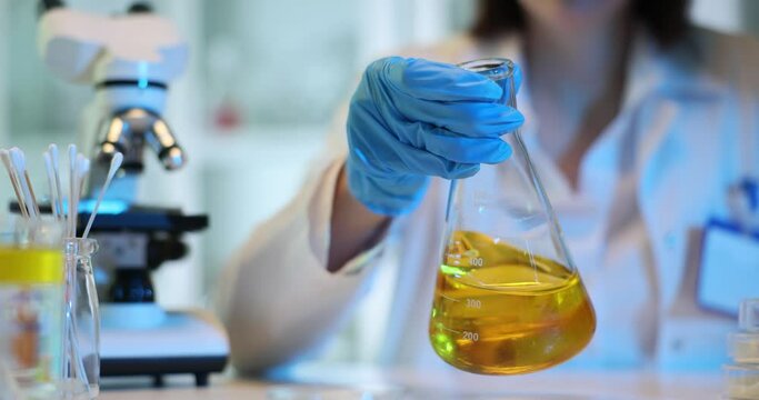 Technician stirs orange liquid in conical flask in lab