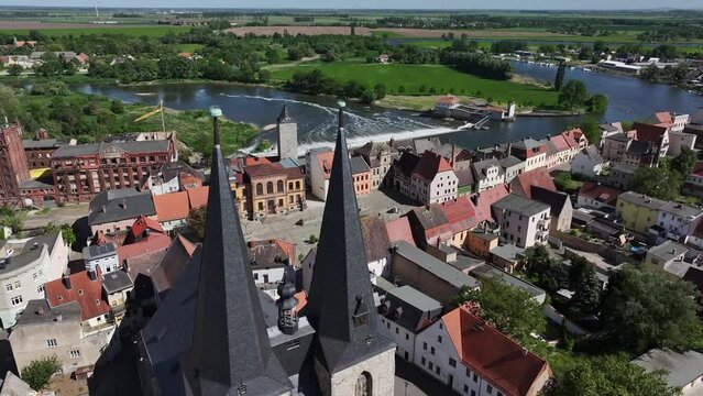 Flight towards the town hall square in Calbe. Movement past the church towers of St. Stefani Church. River Saale and weir in the river in the background. Travel destination in Saxony-Anhalt.