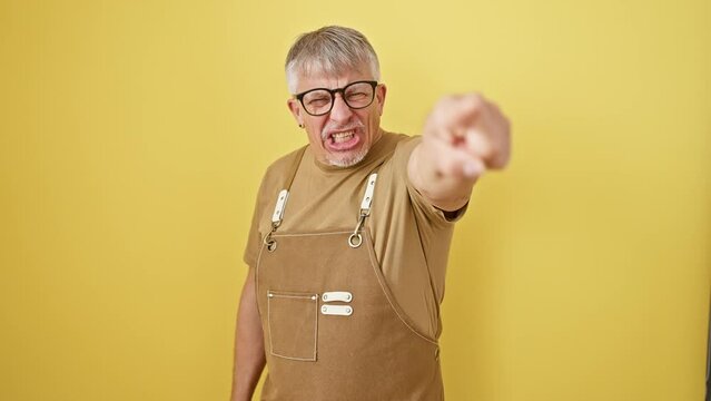 Grey-haired middle-aged man in glasses, sporting an apron, livid in yellow isolation. firing blame from his finger - a mad gesture at the camera, blaming you with unabashed anger.