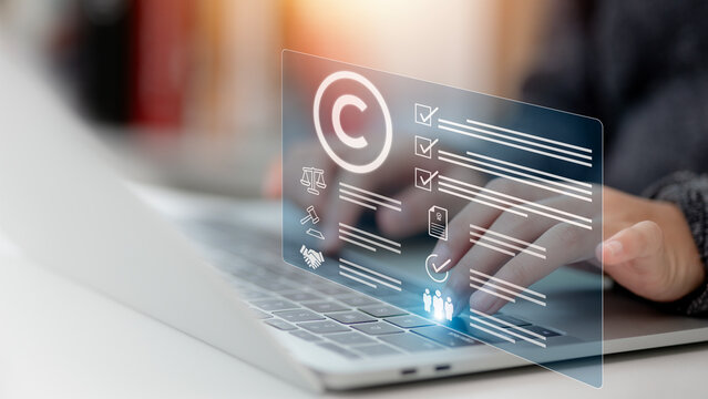 Person's hand using a laptop computer on a futuristic virtual interface screen with a copyright icon background, representing the concept of copyright or patent and creation ownership against piracy c