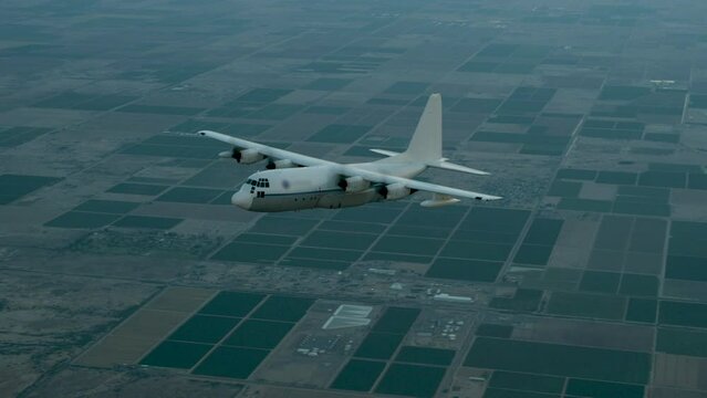Cinematic flying shot around airborne C-130 airplane and skydivers sliding out