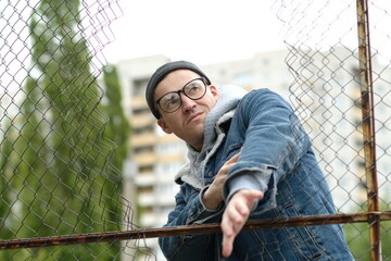 A Man with glasses in a Denim Jacket Dances Near a Chain Link Fence