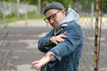 A Man with glasses in a Denim Jacket Dances Near a Chain Link Fence