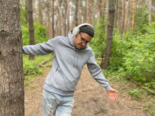 A man in a grey hoodie and headphones dances freely in a forested area. He is lost in his own world, enjoying the music and the feeling of the forest around him.